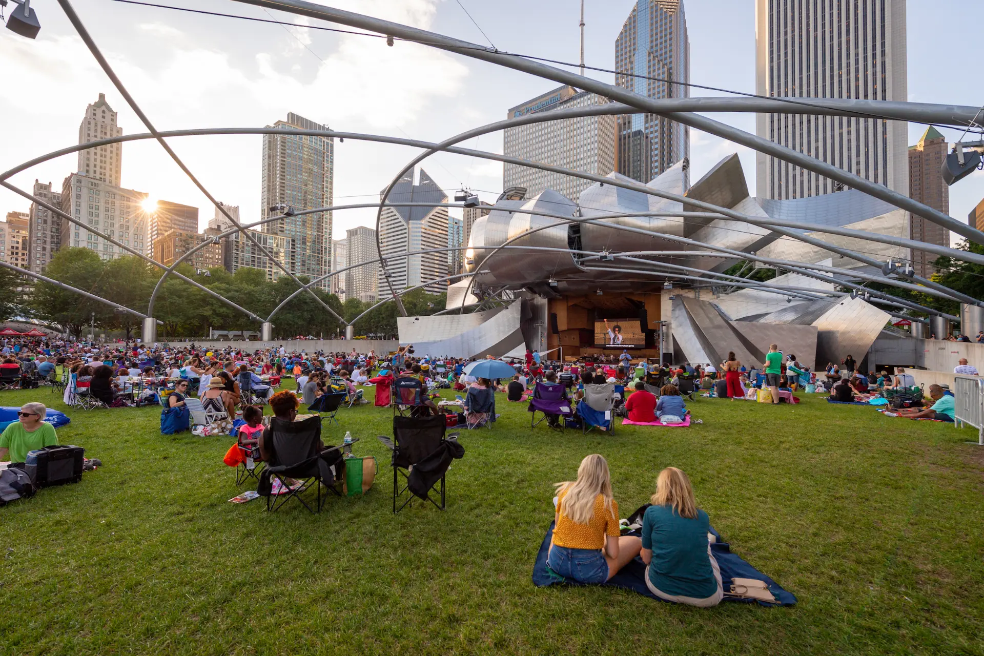 Millennium Park in Chicago, with the Jay Pritzker Pavilion and crowds gathered on the Great Lawn against the downtown skyline